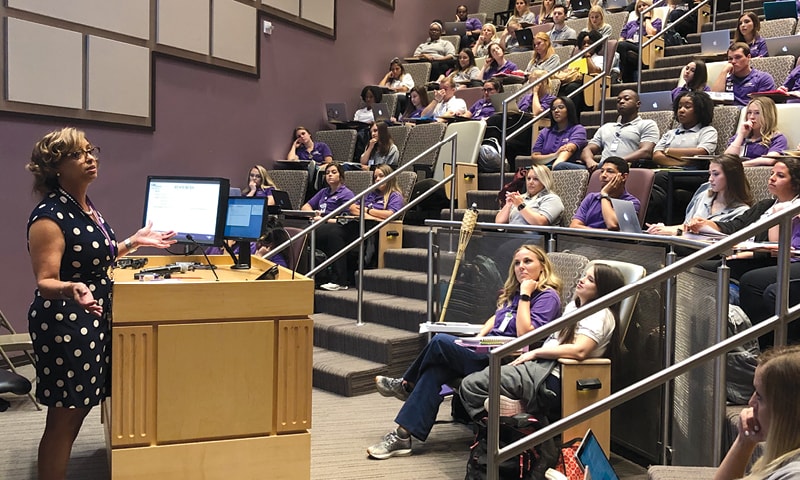 Faculty member Kendra Barrier presenting a lecture to a theater full of nursing students.