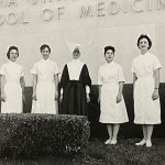 Nursing students pose with a religious sister in a black and white photo from the 1940s.
