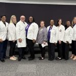 Group of nursing students and faculty in white coats standing together after the White Coat Ceremony at LSU Health Shreveport, smiling in front of a black backdrop.