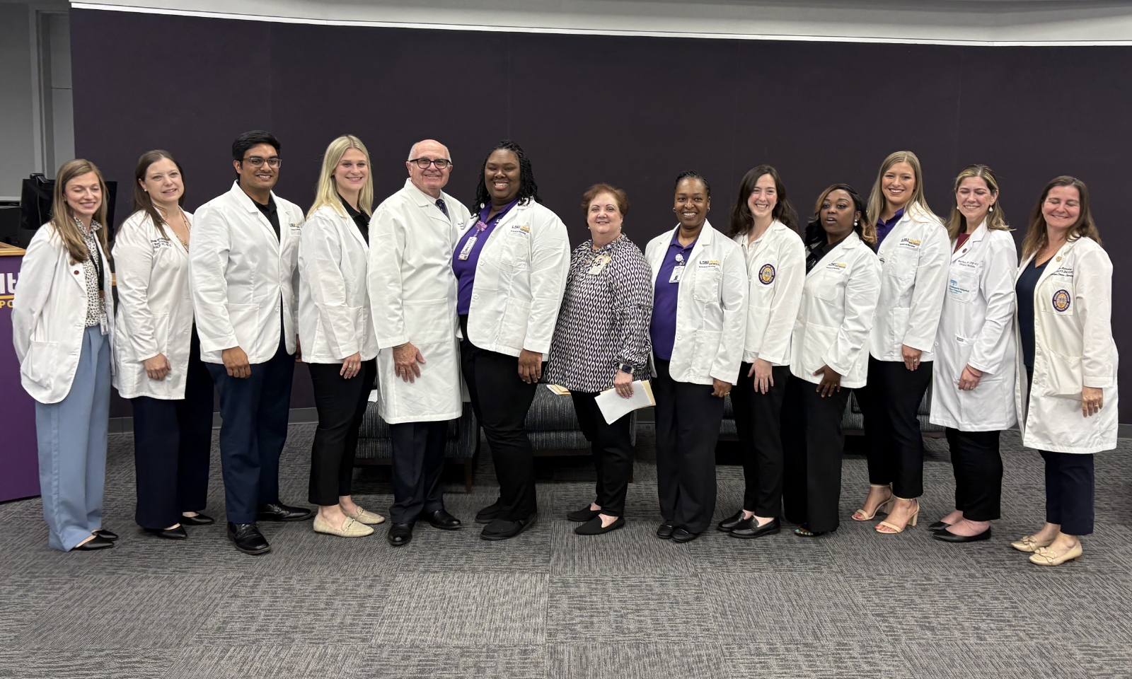 Group of nursing students and faculty in white coats standing together after the White Coat Ceremony at LSU Health Shreveport, smiling in front of a black backdrop.