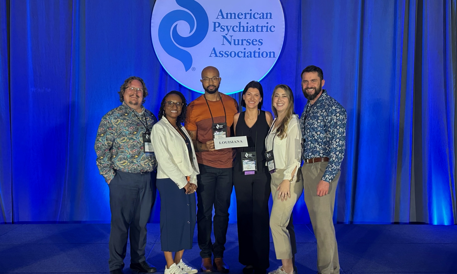 Six LSU Health New Orleans School of Nursing faculty members standing together in front of the American Psychiatric Nurses Association stage backdrop